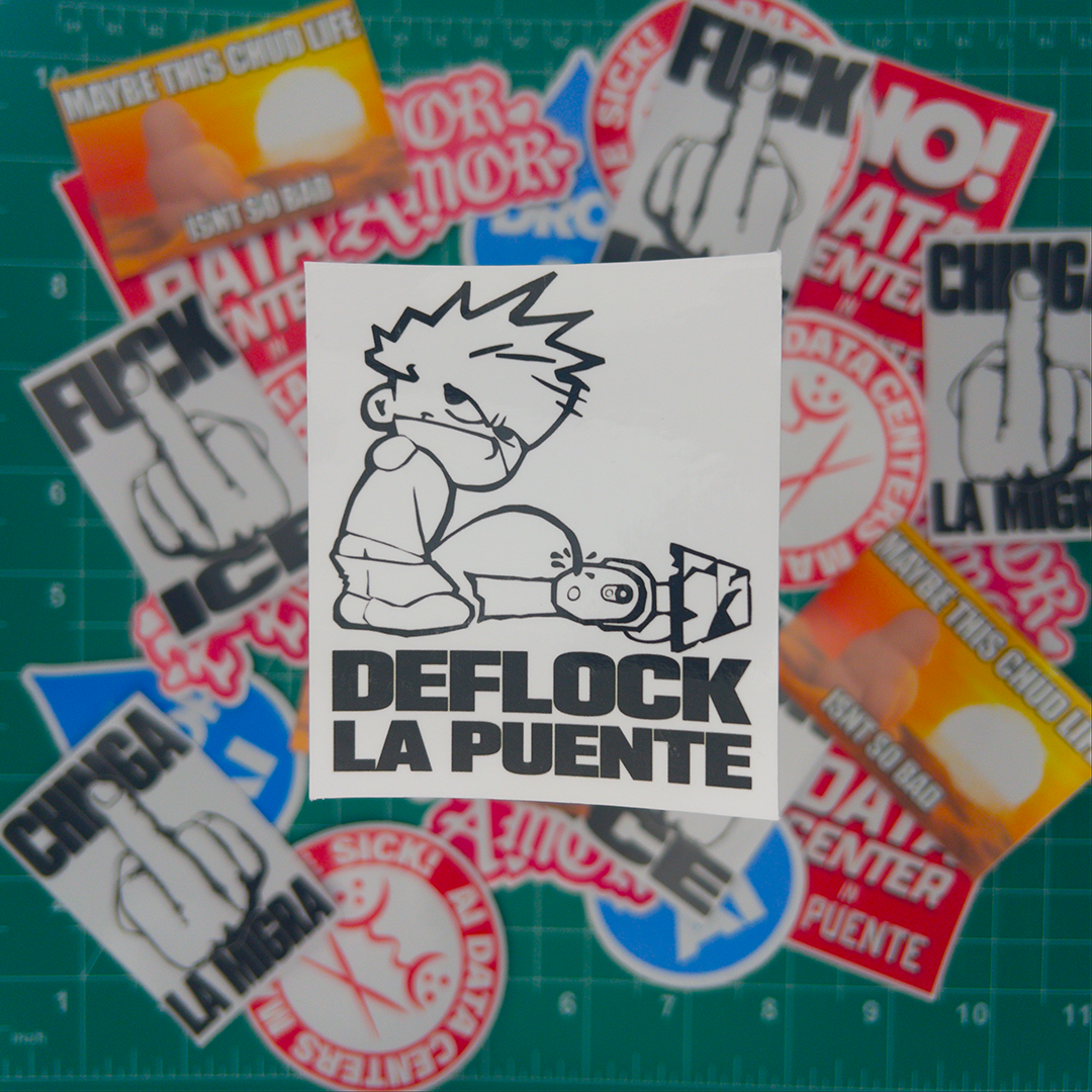 A square white sticker with a black-and-white cartoon drawing and the text 'DEFLOCK LA PUENTE' is centered on top of a scattered pile of similar stickers. The background shows a green cutting mat with grid lines and additional blurred stickers around the edges.