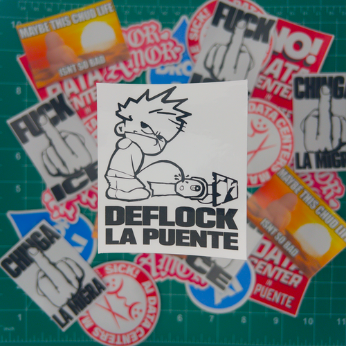 A square white sticker with a black-and-white cartoon drawing and the text 'DEFLOCK LA PUENTE' is centered on top of a scattered pile of similar stickers. The background shows a green cutting mat with grid lines and additional blurred stickers around the edges.